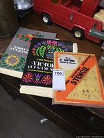 Two vintage stencil books and a package of stencils on a wooden surface with a red toy truck in background.