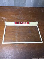 Top front view of the vintage Herco store display topper showing logo and metal frame.