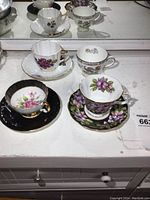 Four teacups with saucers shown, displaying floral patterns and gold accents