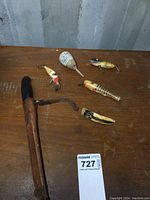 Overview of filet tool with wooden handle and leather sheath, three wooden lures, one wooden float, and one older plastic lure on wooden surface with auction tag.