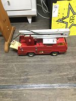Side view of vintage Tonka firetruck showing pressed steel body, white ladder on top, and plastic details with damage.