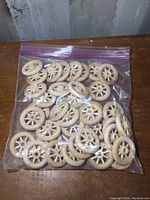 Clear plastic bag filled with approximately 36 wooden toy truck wheels, showing their spoked design, light wood color, and round shape.
