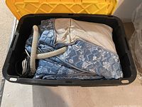 Photo showing the queen air mattress folded inside a black and yellow plastic tote with the attached electric pump hose.