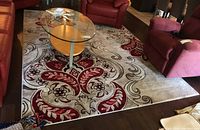 Full view of the beige and red floral patterned area rug placed among red leather sofas and glass coffee table