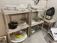 Shelf holding various white Corningware dishes, clear glass bakeware including Pyrex, bowls, plates, and baking trays for kitchenware lot.