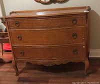 Front view of wooden three drawer dresser showing curved drawer fronts, metal ring handles, and carved detailing on legs and bottom edge.