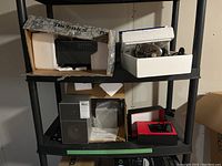 Front view of items on shelving including Technics receiver in original box, Huawei wireless terminal, Yamaha speaker, and Koss headphones in foam packaging.