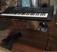 Full view of keyboard on X-style metal stand with cover and adapter visible