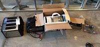Photo showing all items together: toaster, coffee maker in box, car battery charger/starter, door lock hardware.