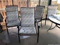 Set of six aluminum patio chairs arranged on a patio, showing front view with light geometric cushions and dark frames.