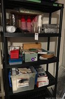 Wide shot of three black plastic shelves containing various picnic ware including disposables, aluminum trays, paper goods, plastic cutlery and totes.