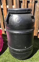 Front of black plastic rain barrel with horizontal ribs and attached spout at top.
