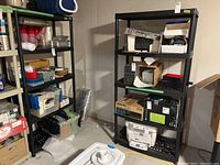 Two black resin shelving units side by side in basement with miscellaneous storage items on shelves