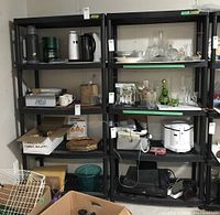 Front view of two black resin shelving units filled with various household items, showing five shelves each and the slatted shelf design.