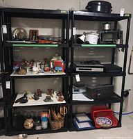 Two black resin shelving units side by side with various household items on the shelves, demonstrating shelf structure and color.