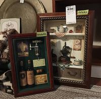 Two shadow boxes positioned upright; one shows wine-themed miniatures with wine bottles, corkscrew, cork, and labels, the other displays kitchen-themed items such as coffee grinder and cups.