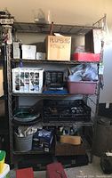 Front view of steel shelving unit loaded with assorted items including boxes, plastic bins, and containers labeled 'PLUMBING & CAULK'.