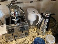 Photo of Hamilton Beach toaster, silver cream pitcher on top, Brita filter pitcher, and silver coffee carafe on kitchen countertop.