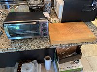 Full view of Black & Decker toaster oven next to wooden cutting board on kitchen counter.