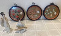 Photo showing three round Asian imitation jade wall hangings with floral motifs and two Asian figurines arranged on a table.