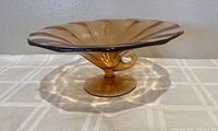 Side view of amber swirl art glass bowl on pedestal base, showing fluted edges and concave center.