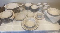 Full view of 72-piece Noritake Blossom Time ivory china set arranged on a table with stacks of plates, bowls, cups, saucers, and serving pieces.
