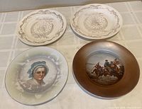 Four commemorative plates laid out on a table: two George Washington plates with laurel wreath border, one Martha Washington portrait plate, and one George Washington crossing the Delaware plate with brown rim.