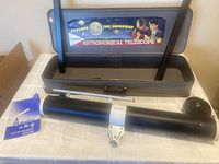 Photo of the telescope hard case with illustrated label, carrying handle visible, includes the telescope and instruction manual on the table.