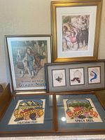 Four framed artworks displayed against a wall: color giclee print, Grape Nuts poster, two embroidered fruit labels, and a framed triptych of embroidered hats