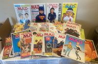 Shows a selection of MAD magazines with various covers including Alfred E. Neuman and Batman themed covers. Magazines are arranged standing and laid out flat, each in protective bags.