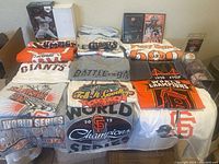 Display of 14 varied San Francisco Giants T-Shirts spread out on a surface, showing logos and championship years