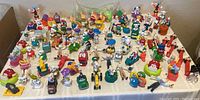 Wide overhead view showing an array of vintage McDonald’s toys including many Dalmatian figures, M&M characters, Tonka truck sealed in original packaging, Pez dispenser and other miniature toys arranged on a white cloth-covered surface.