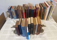 Front view of all 43 books arranged on table with the two sets of duck bookends at each end of the row.
