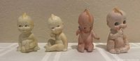 Front view of four small Kewpie dolls in a row on a white surface, showing condition and colors