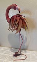 Full side view of the pink metal flamingo showing layered feathers, rust spots and paint wear on one side.