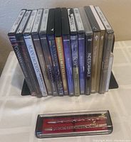 Full view of 13 DVDs and 1 CD featuring religious, biblical, and gospel titles, all standing vertically with spines visible, with a pen and pencil set in a clear plastic box in front.
