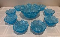 Full view of the dessert set with one large bowl placed in center surrounded by eight smaller bowls, all in turquoise blue textured glass