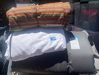 Photo showing the camping mat rolled or folded, white duvet, and colorful striped toddler blanket stacked together.