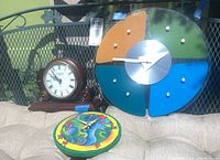 Three clocks on a bench: wooden mantle clock, colorful artistic clock, and large modern segment clock