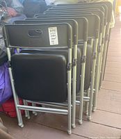 Stack of ten black COSCO plastic folding chairs showing folded position and seat surfaces.