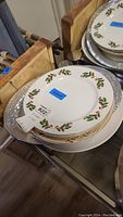 Stack of assorted plates including white ones with red and green holly pattern around the edge
