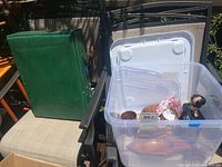 Photo showing green folding stool on chair with plastic bin containing wood dishes, mugs, and vintage decanter