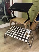 Black adjustable laptop desk with tilting top and foldable legs sitting on a wooden side table, next to black and white polka dot foldable laptop desk