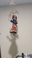 Full view of the marionette puppet hanging against a wall, showing body, strings, and wooden control bar.