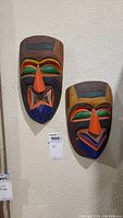Both colorful wooden masks mounted on wall next to each other showing their full form and size.