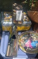 Photo showing three decorative metal boxes stacked and arranged with a tall metal vase with heart-shaped cutout and a round painted metal tray