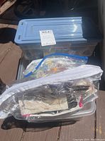 Two small plastic bins containing various sewing notions, visible threads, buttons, zippers, and other sewing accessories packed inside and in ziploc bags.