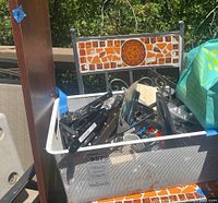 Box holding various metal shelving brackets and wooden boards on a mosaic-tiled shelf bench outdoors