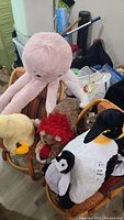 Photo showing five stuffed animals on chairs including a pink octopus, penguin with baby penguin, lamb, brown dog with red scarf, and yellow duck.