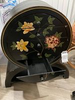 Front view of vintage short round wooden cabinet with hand-painted floral design and drawers partly open showing removable drawer.